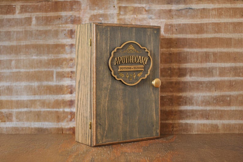 Corner view of rustic wooden apothecary-style box with bronze and gold accents with 'Apothecary Potions & Elixirs' label on a wooden background