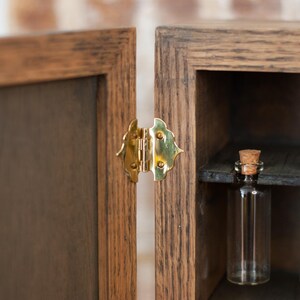 close up view of gold hinge on rustic wooden apothecary box with glass vials hanging on shelf