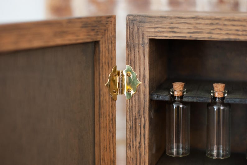 close up view of gold hinge on rustic wooden apothecary box with glass vials hanging on shelf