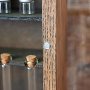 close up of rustic wooden apothecary-style box with bronze and gold accents, glass vials and jars in various sizes with 'Apothecary Potions Elixirs' sign on a wooden tabletop and brick background