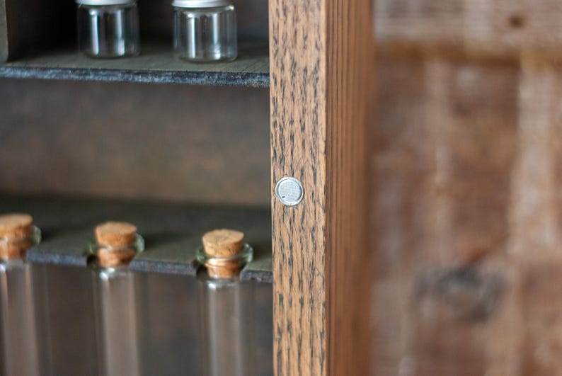 close up of rustic wooden apothecary-style box with bronze and gold accents, glass vials and jars in various sizes with 'Apothecary Potions Elixirs' sign on a wooden tabletop and brick background