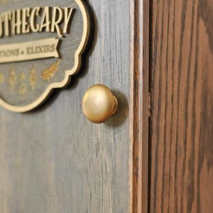 Close up view of bronze gold knob on a rustic wooden apothecary-style box with 'Apothecary Potions & Elixirs' sign