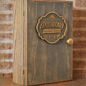 Corner view of rustic wooden apothecary-style box with bronze and gold accents with 'Apothecary Potions & Elixirs' label on a wooden background