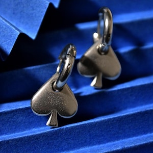 May include: A pair of silver hoop earrings with a spade-shaped charm hanging from each hoop.