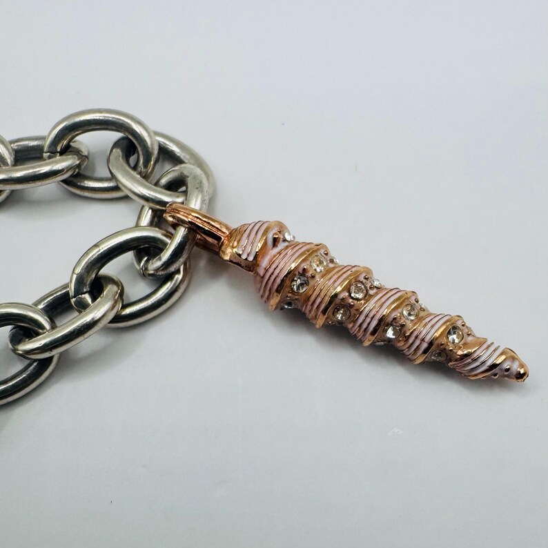 May include: A silver-toned chain link bracelet featuring a single pendant shaped like a spiral seashell. The pendant is finished in rose gold and white enamel, accented with small, clear, round-cut crystals embedded along the spiral ridges.