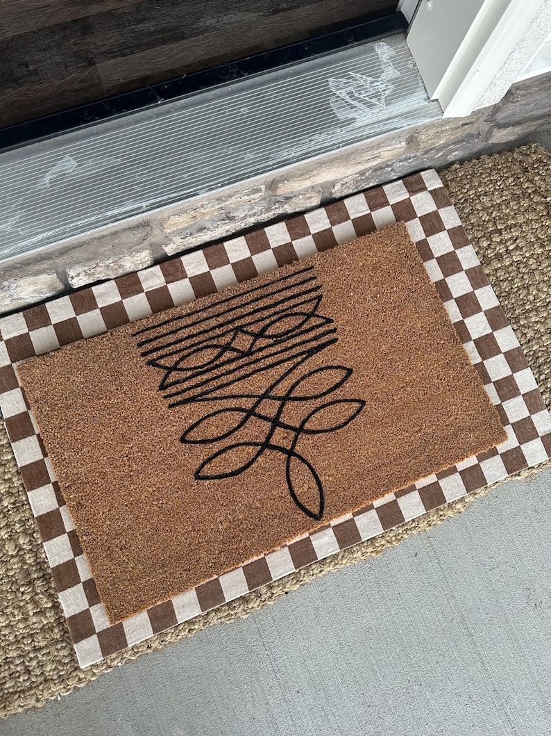 Peut inclure: Un paillasson en fibre de coco brun avec un motif abstrait noir. Le paillasson est pos&eacute; sur un tapis &agrave; carreaux.
