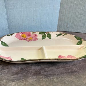 Puede incluir: Plato ovalado dividido para servir con base color crema. El plato está decorado con diseños florales rosas y hojas verdes. El borde tiene un ribete marrón. El plato está dividido en tres secciones.