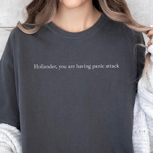 Może przedstawiać: Ciemnoszara koszulka z białym napisem "Hollander, you are having panic attack". Koszulka ma okrągły dekolt i luźny krój. Słowo "PEPPER" znajduje się na dole obrazu.