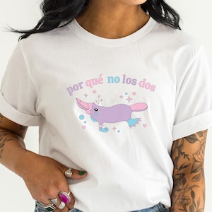 Puede incluir: Camiseta blanca con un ornitorrinco de dibujos animados con una corona y el texto "por qué no los dos" en letras rosas y azules.