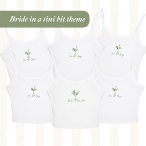Könnte beinhalten: Weiße Tanktops mit dünnen Trägern. Jedes Oberteil zeigt eine grüne Illustration eines Martiniglases mit einer Person darin. Der Text "you bet tipsy" und "Bride in a tini bit theme" sind ebenfalls sichtbar.