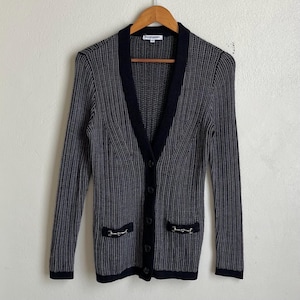 May include: A black and white striped cardigan with a black trim and silver hardware. The cardigan has a v-neck and button closure.