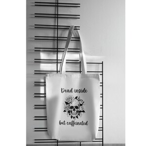 Puede incluir: Bolsa de tela blanca con texto negro y un gráfico de calavera. El texto dice "Dead inside but caffeinated".