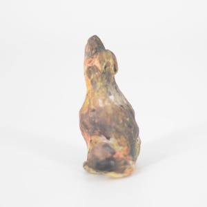 May include: A ceramic sculpture of a bird with brown, orange, and yellow paint. The bird is perched on a white surface.