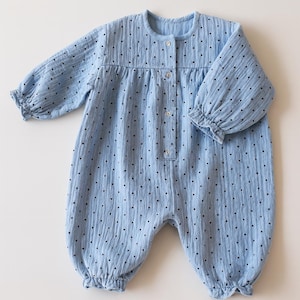 May include: A pale blue baby romper with long sleeves and a round neck. The romper features small, evenly spaced black dots. The sleeves and ankles have a frilled trim, and the front has button fastenings.