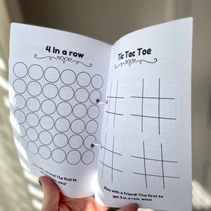 K&ouml;nnte beinhalten: Ein schwarz-wei&szlig;es druckbares Spielheft mit zwei Spielen: 4 in einer Reihe und Tic Tac Toe. Das Heft ist auf der Tic Tac Toe-Seite ge&ouml;ffnet, die ein Gitter mit Linien f&uuml;r die Spieler zum Markieren ihrer Felder hat.