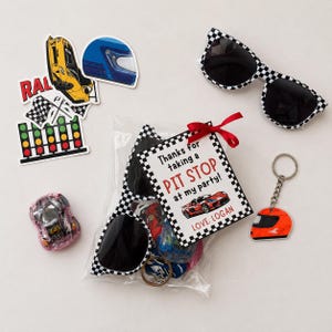 Puede incluir: Un conjunto de recuerdos de fiesta con tem&aacute;tica de carreras. Incluye gafas de sol a cuadros, un llavero con un casco naranja, pegatinas y una bolsa de golosinas con una etiqueta que dice "Thanks for taking a PIT STOP at my party!"