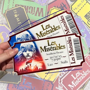 Puede incluir: Dos entradas para el musical "Les Misérables" en el Teatro Sondheim, con un retrato de una joven con una bandera roja. Las entradas son blancas con letras doradas y un código de barras.