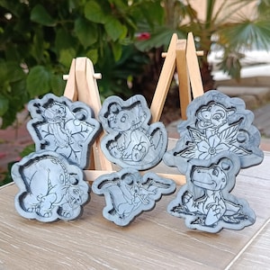 Könnte beinhalten: Eine Sammlung grauer, cartoonartig geformter Tierformen. Die Formen zeigen verschiedene Tiere, darunter einen Dinosaurier, einen Frosch und einen Löwen. Die Formen werden auf einer Holzoberfläche präsentiert.