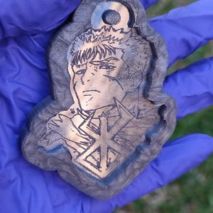 Könnte beinhalten: Ein Holzschlüsselanhänger mit einem Schwarzweißbild eines Charakters aus der Anime-Serie Berserk. Der Charakter hat stacheliges Haar und hält ein Schwert. Der Schlüsselanhänger hat oben ein Loch zum Anbringen an einem Schlüsselring.