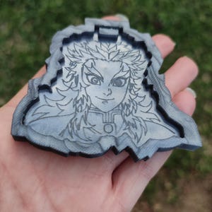 Könnte beinhalten: Ein grauer Holzausschnitt eines Charakters aus dem Anime Demon Slayer. Der Charakter hat langes, weißes Haar und trägt eine dunkle, gemusterte Robe. Der Ausschnitt ist detailliert und hat eine strukturierte Oberfläche.