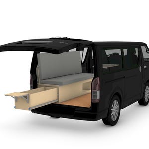 May include: A black van with its rear hatch open, revealing a light wood interior conversion. The setup includes a gray cushioned bench seat and a pull-out wooden drawer unit that extends from the back, featuring a flat surface top.