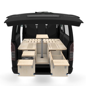 May include: A black van with the back door open, revealing a custom-built wooden interior with a table, drawers, and a bed platform. The interior is designed for camping and includes a small stove.