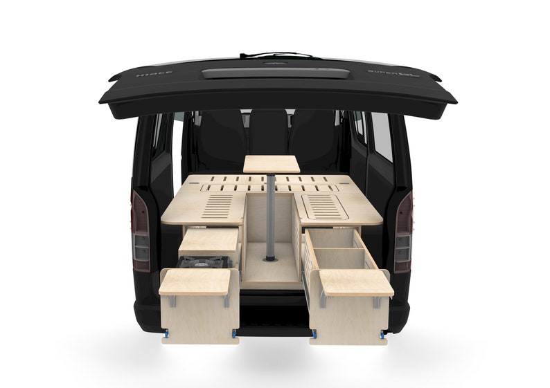 May include: A black van with the back door open, revealing a custom-built wooden interior with a table, drawers, and a bed platform. The interior is designed for camping and includes a small stove.