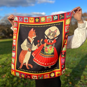 Può includere: Una sciarpa quadrata rossa e nera con un bordo colorato che presenta un gatto in abito che tiene un fiore e un gatto in un vestito rosso che tiene un mazzo di fiori. Lo sfondo è nero con un motivo a pois bianchi.