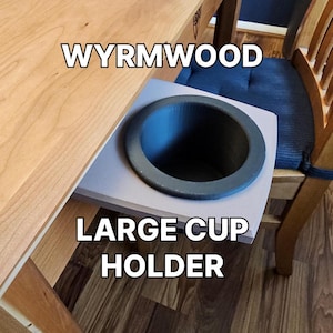 May include: A wooden table with a large cup holder attached to the side. The holder is made of a light gray material and has a black rubber insert. The text "WYRMWOOD LARGE CUP HOLDER" is printed on the table.
