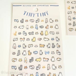 May include: Clear sticker sheet featuring numerous cartoon cat illustrations in various poses and colors. The text "TINY TINY" is above the stickers, with "RELAXED AND COMFORTING" above that. The sticker sheet is on a white background.
