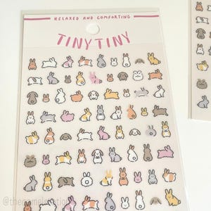 May include: A sheet of clear stickers featuring tiny illustrations of rabbits, dogs, and other animals in various colours. The stickers are arranged in rows and columns on a white background. The text "Tiny Tiny" and "Relaxed and Comforting" are printed at the top of the sheet.