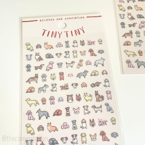 Peut inclure: Une feuille d'autocollants représentant une variété d'illustrations de chiens mignons dans différentes poses et couleurs. Les autocollants sont disposés en rangées et en colonnes sur un fond blanc. Le texte "Tiny Tiny" est imprimé en haut de la feuille, ainsi que la phrase "Relaxed and Comforting".