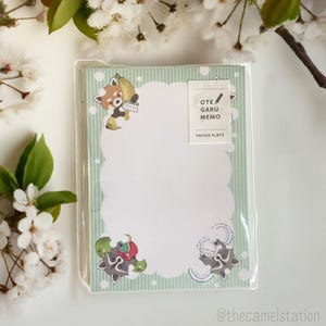 May include: A pack of green and white memo pads with a red panda illustration. The memo pads have a cloud-shaped note area with a white background and a green and white striped border. The text on the memo pad says "OTE GARU MEMO PAPIER PLATZ".