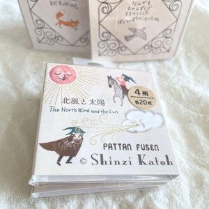 May include: A square pack of Pattan Fusen sticky notes featuring The North Wind and the Sun illustration by Shinzi Katoh. The design includes a pink sun, a person on a horse, and a figure in a cloak. A circular sticker indicates 4 patterns, 20 sheets each.