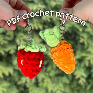 Puede incluir: Dos llaveros de ganchillo: una fresa roja con hojas verdes y una zanahoria naranja brillante con hojas verdes. Ambos están unidos a llaveros plateados. El texto "PDF crochet pattern" está arqueado encima.