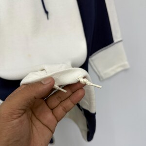 Puede incluir: Sudadera con capucha blanca y azul marino con el texto "courr&egrave;ges paris" en gris. La sudadera tiene un cord&oacute;n y un panel azul marino en contraste en el lateral. Los pu&ntilde;os son blancos.