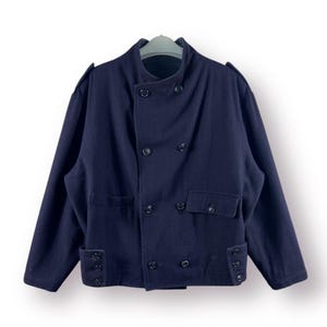 Könnte beinhalten: Eine dunkelblaue, zweireihige Jacke mit Stehkragen und mehreren Knöpfen. Die Jacke hat zwei Pattentaschen und eine einzelne Tasche auf der linken Seite.