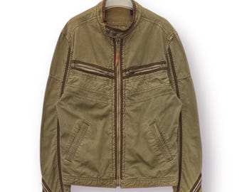 May include: A tan jacket with a brown collar and trim. The jacket has a zipper closure, multiple zippered pockets, and a small leather tag. The sleeves have brown stripes near the cuffs. The jacket is hanging on a white hanger.