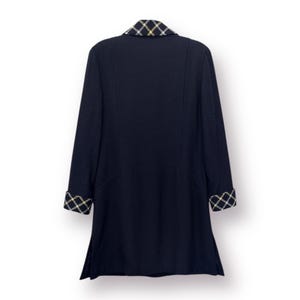 May include: A navy blue coat with a contrasting plaid collar and cuffs. The coat has long sleeves and a tailored fit. The plaid pattern incorporates black, white, and gold colors. The coat is shown against a white background.