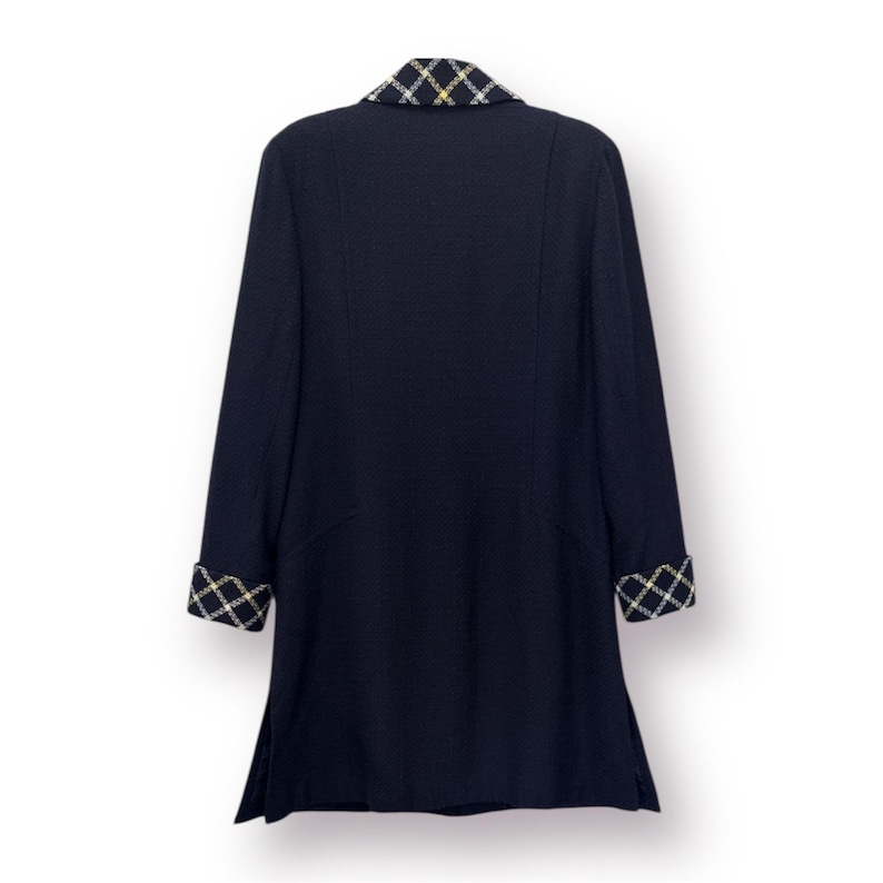 May include: A navy blue coat with a contrasting plaid collar and cuffs. The coat has long sleeves and a tailored fit. The plaid pattern incorporates black, white, and gold colors. The coat is shown against a white background.
