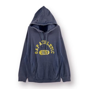 以下が含まれることがあります： GAP ATHLETIC 1969と黄色のグラフィックがプリントされた濃い青色のフード付きスウェットシャツです。