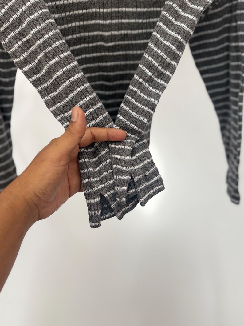 May include: A long-sleeve shirt featuring a ribbed texture with a pattern of horizontal dark gray and white stripes. The sleeves are designed with a small vertical slit at the cuff, providing a distinct detail to the garment's overall construction.