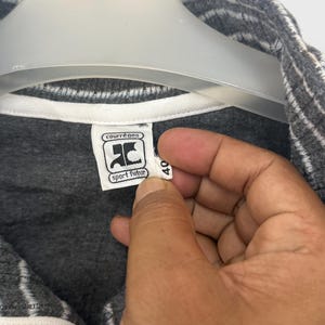 May include: A dark gray zip-up jacket with white pinstripes and a white inner collar lining. The garment features a white interior brand label with the text courr&egrave;ges sport futur and a small white size tag with the number 40 attached to the collar.