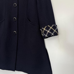 May include: A navy blue coat with a textured fabric. The coat features four round buttons and a plaid pattern on the sleeve cuffs. The coat has a classic design with a tailored fit and pockets.