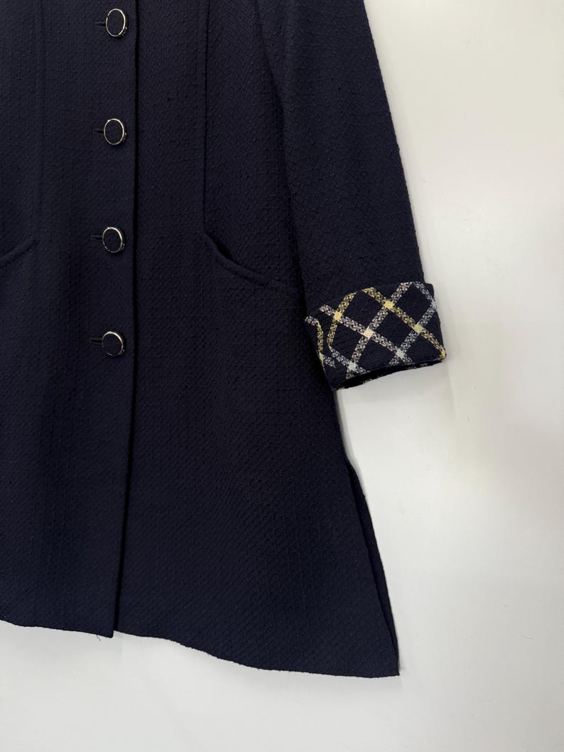 May include: A navy blue coat with a textured fabric. The coat features four round buttons and a plaid pattern on the sleeve cuffs. The coat has a classic design with a tailored fit and pockets.