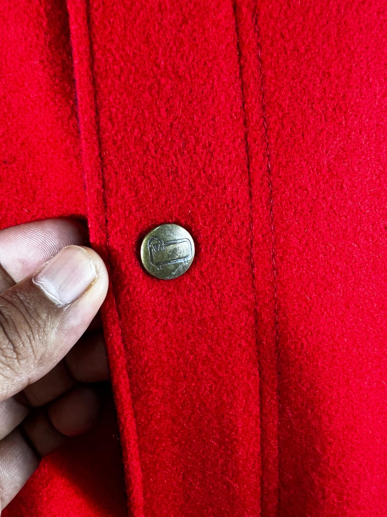 May include: A close-up of a red fabric jacket with a gold button. The button has a small logo on it.