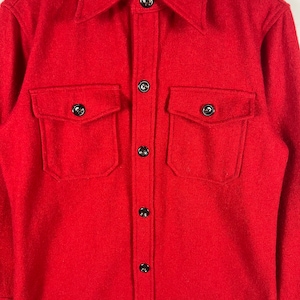 May include: A red wool shirt with a button-down collar and two large flap pockets. The shirt has a label that reads "Pendleton"
