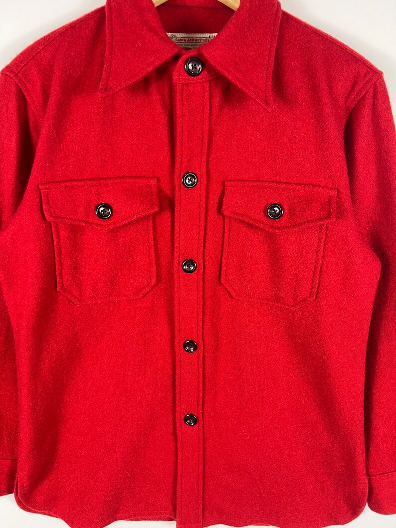 May include: A red wool shirt with a button-down collar and two large flap pockets. The shirt has a label that reads "Pendleton"