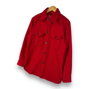 May include: A red long-sleeved button-up shirt with two large flap pockets on the front. The shirt is made of a soft, textured fabric.