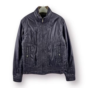 Könnte beinhalten: Dunkelmarineblaue Steppjacke mit hohem Kragen und durchgehendem Reißverschluss. Die Jacke hat zwei Vordertaschen mit Knopfverschlüssen und ein Rautenmuster. Die Jacke ist etwa 71 cm lang.